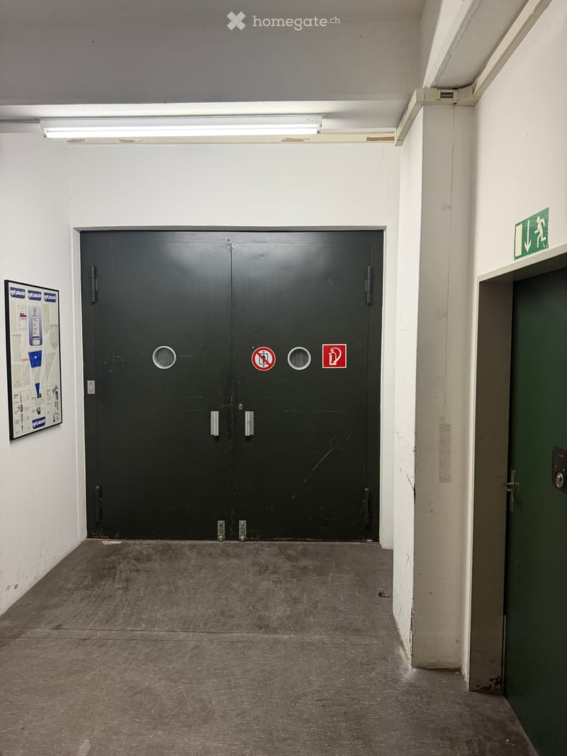 Empty hallway with a large black garage door, white walls, and a concrete floor.
