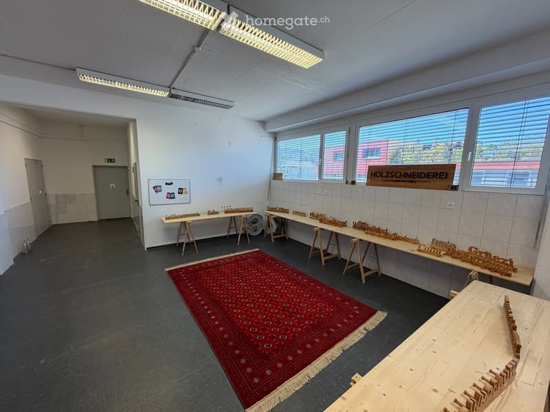 Bright, open room with large windows, wooden tables on stools, red patterned rug, and wooden sign on wall.