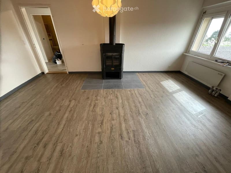 Empty room with wooden flooring, fireplace, large windows, and a hanging light fixture.
