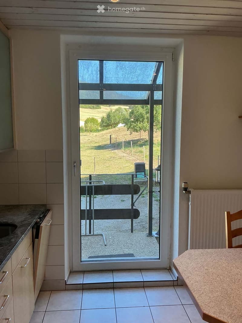 Bright kitchen with tiled floor, granite countertop, and a large sliding glass door opening to a patio with a scenic view of a green field and trees.