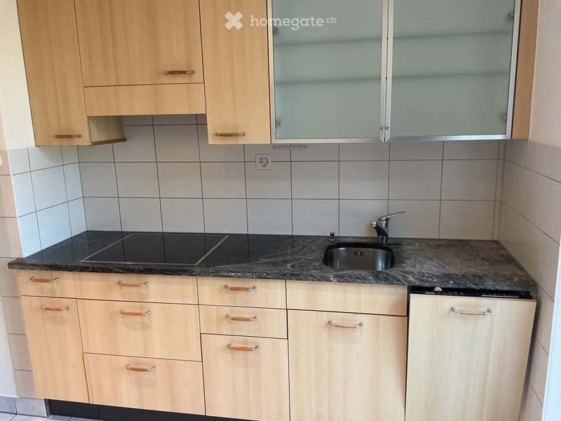 Modern kitchen with light wooden cabinets, granite countertop, sink, and built-in appliances.