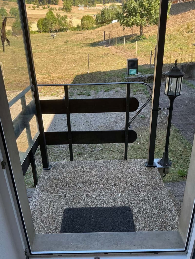 Balcony with metal railing, gravel flooring, and a view of a grassy field with trees and a lamppost.