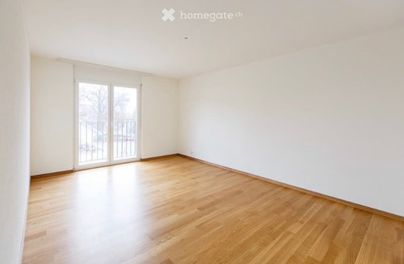 Empty room with wooden flooring, white walls, and large sliding glass doors leading to a balcony.