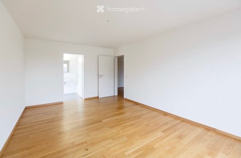 Empty room with light wooden flooring and white walls, featuring three open doors leading to other spaces.