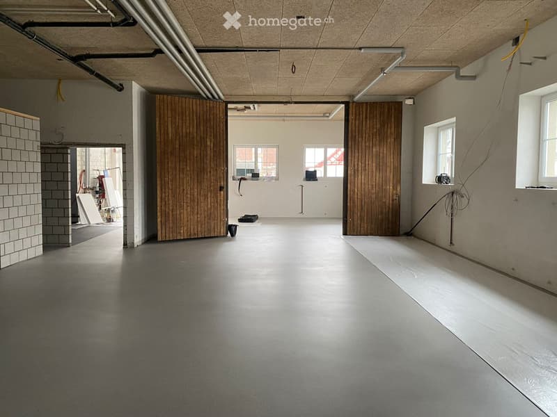 Empty room with concrete floors, exposed wooden doors, and natural light from windows. No furniture or equipment present.