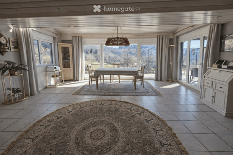 large living room with dining area, large windows, carpet, table and chairs, rug, wooden cabinet, printer, clock, plants