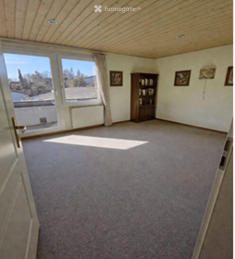 empty room, carpeted floor, large window, wooden ceiling, bookshelf, picture frames
