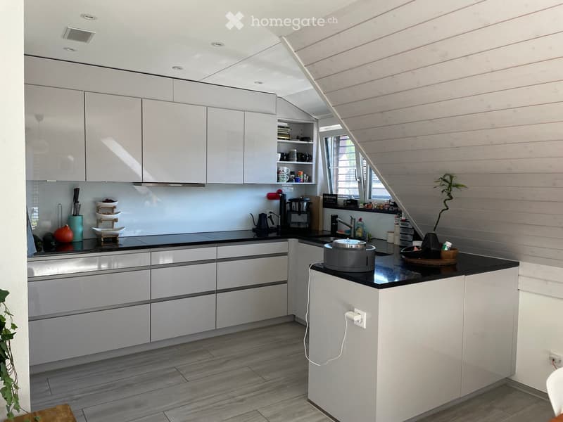 Modern kitchen with white cabinets, black countertops, and various appliances including a coffee maker, teapot, and sink.