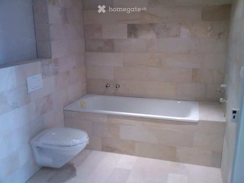 Modern bathroom with a bathtub, toilet, and beige tiled walls and floor.
