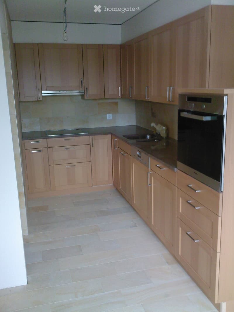 Modern kitchen with light wooden cabinets, stainless steel oven, and tiled floor.