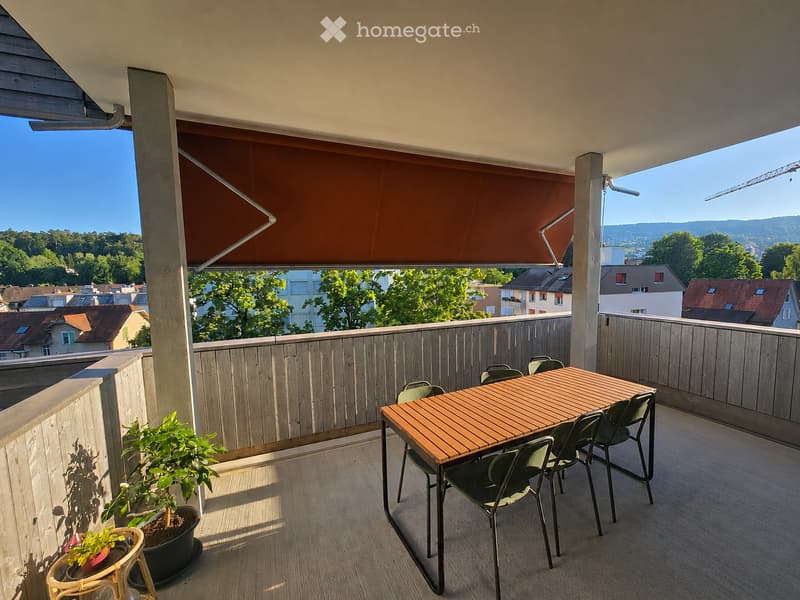 Balcony with wooden decking, a table and chairs, potted plants, and a view of the city and surrounding landscape.