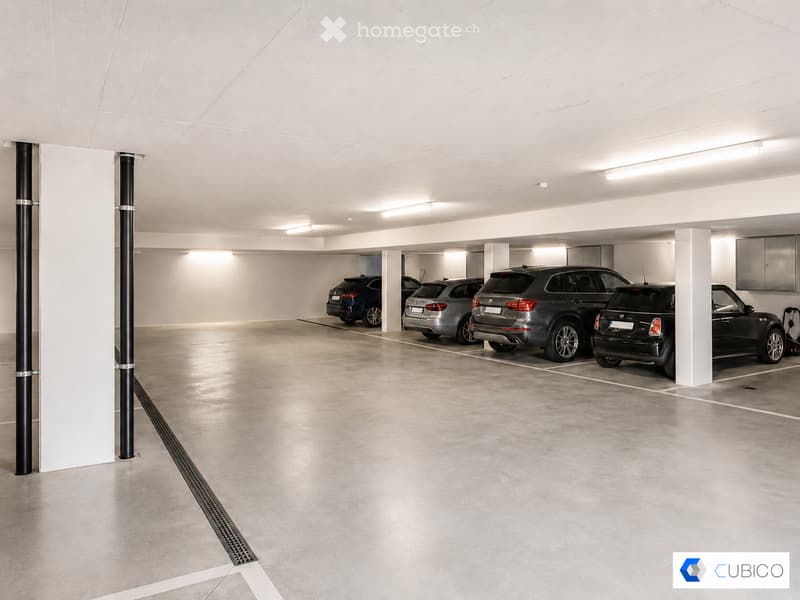 Underground parking area with several parked cars, white walls, and a clean, organized space.