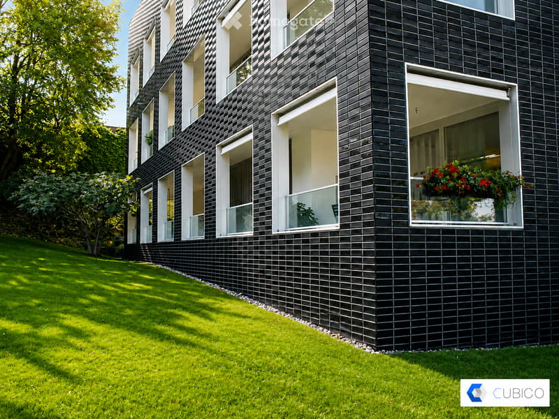Modern multi-story building with black tiled facade, large windows, and balconies with flower boxes.