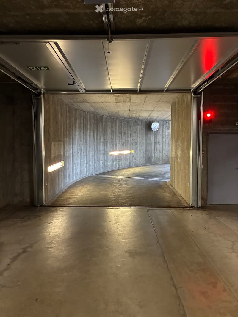 Empty concrete corridor with industrial lighting, red emergency lights, and a visible fire exit sign.