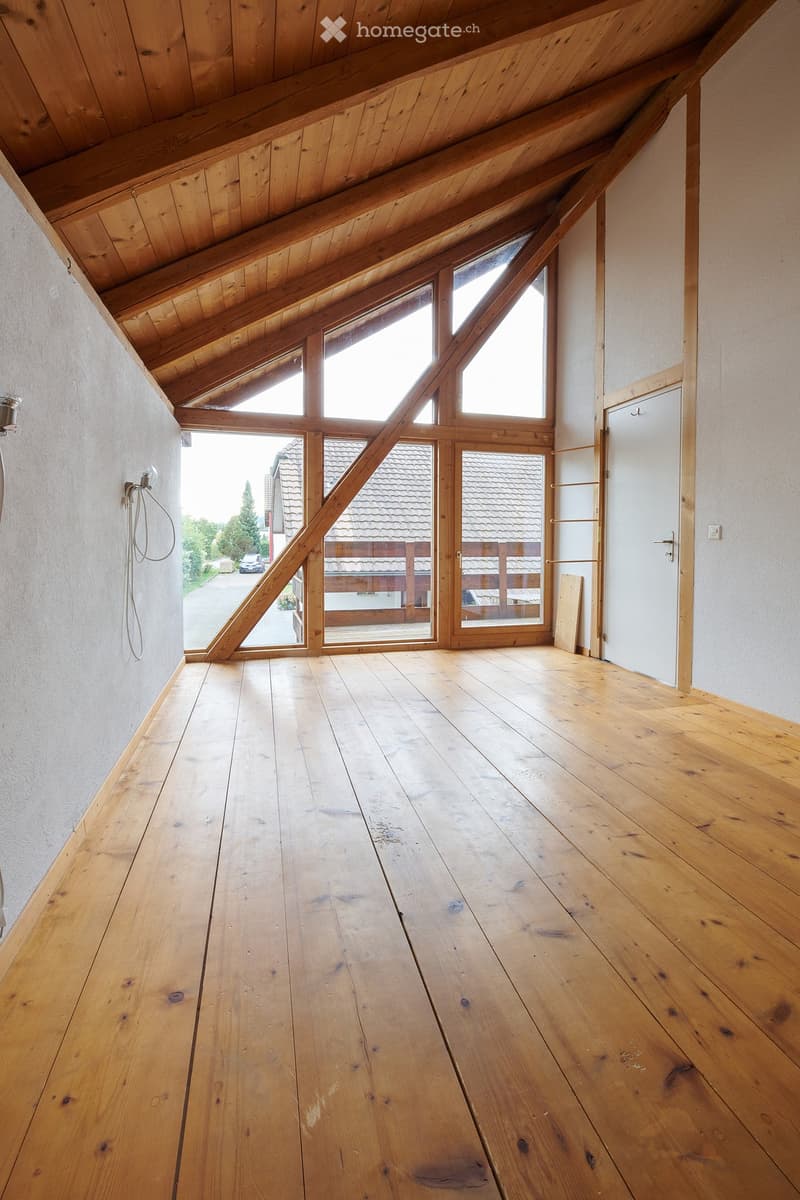 Empty attic space with wooden floors, exposed wooden beams, large skylights, and a door leading to an outdoor deck.