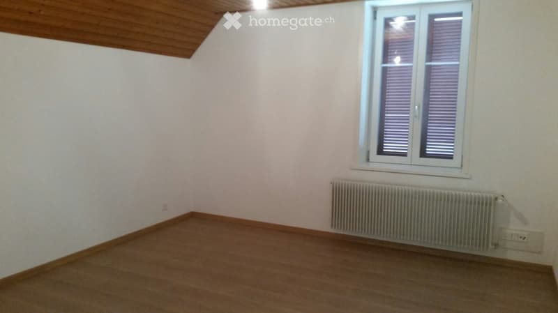 Empty room with wooden flooring, white walls, a window with blinds, and a radiator below the window.