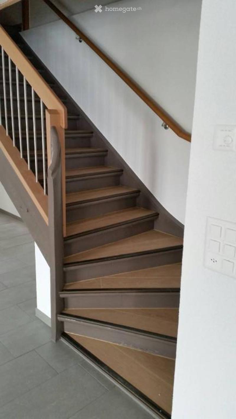 Modern staircase with wooden steps and handrails, white walls, and tiled floor.
