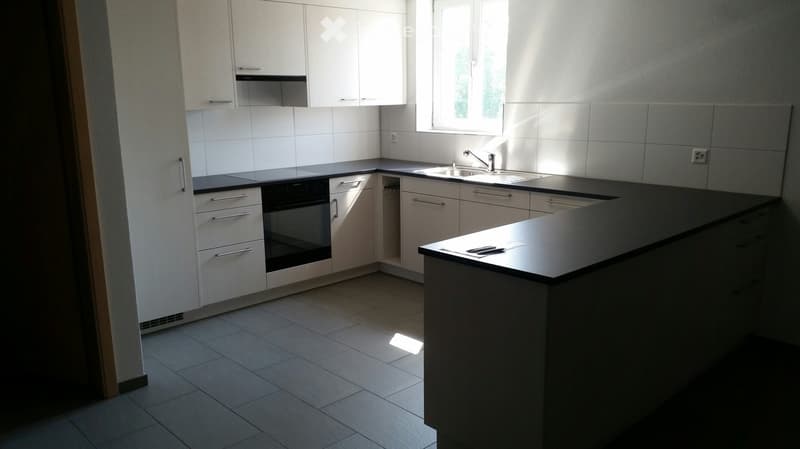 Modern kitchen with white cabinets, black countertops, and a central island. Features include a sink with a faucet, an oven, and ample storage space.