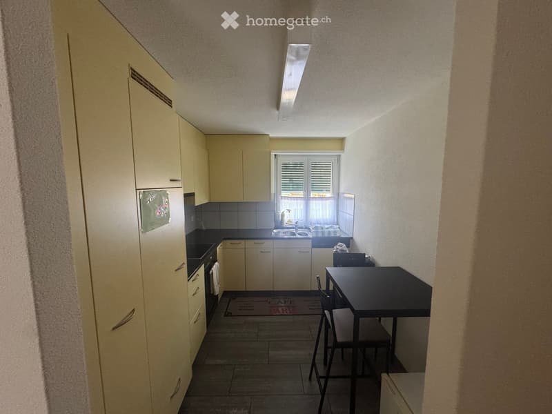Compact kitchen with light-colored cabinets, a sink, an oven, and a small dining area with a table and chairs.