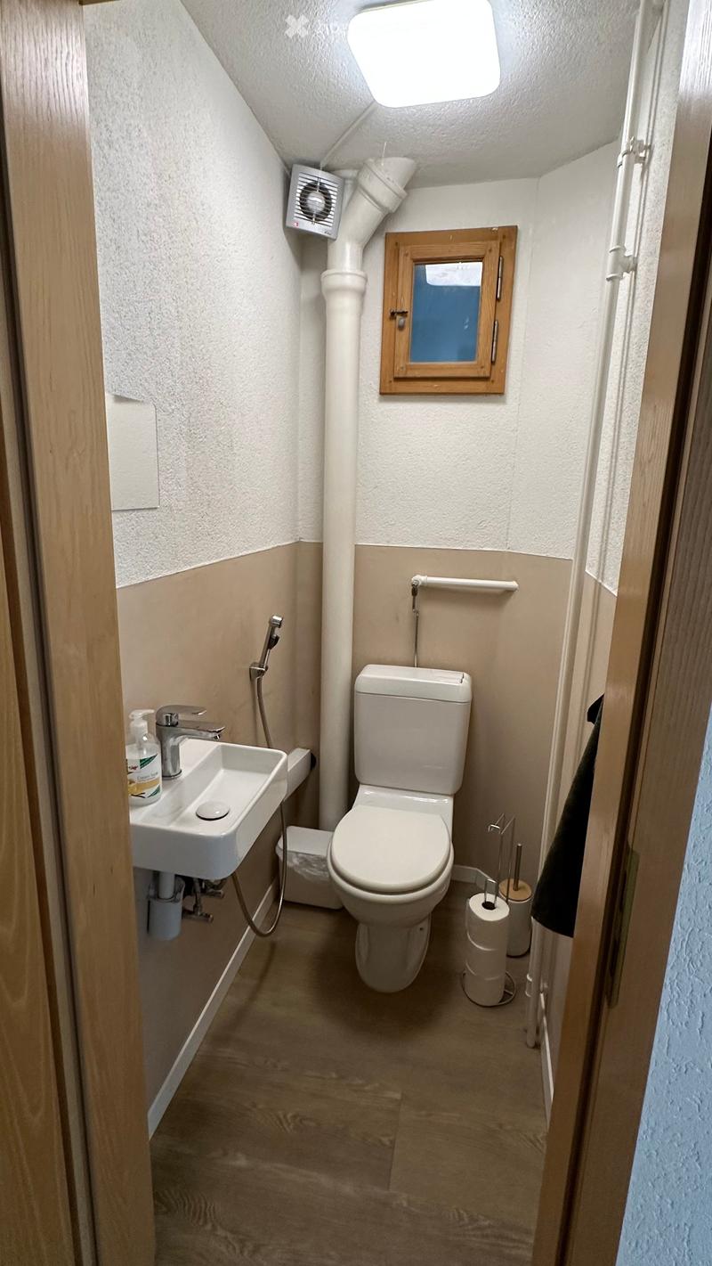 Compact bathroom with a toilet, sink, and small window. Includes a handrail, fan, and toilet paper holder.