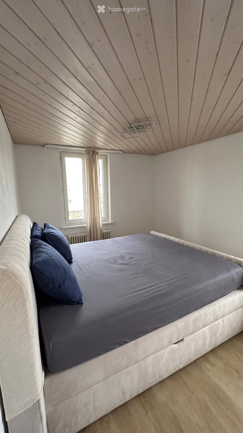 Bedroom with a single bed, blue bedding, and pillows, set against white walls and wooden flooring.