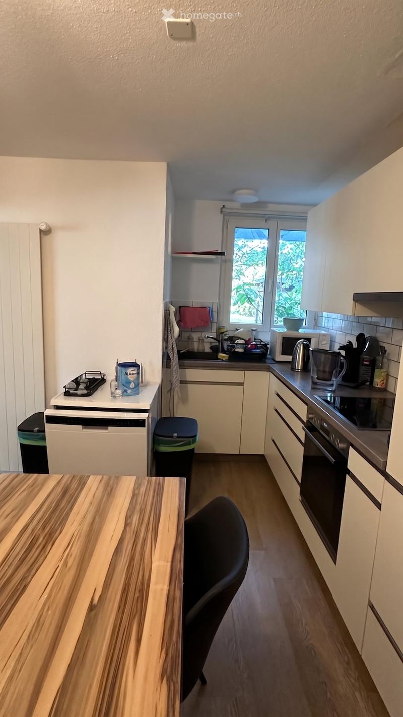 Modern kitchen with white cabinets, wooden table, black chair, microwave, oven, dishwasher, and sink.