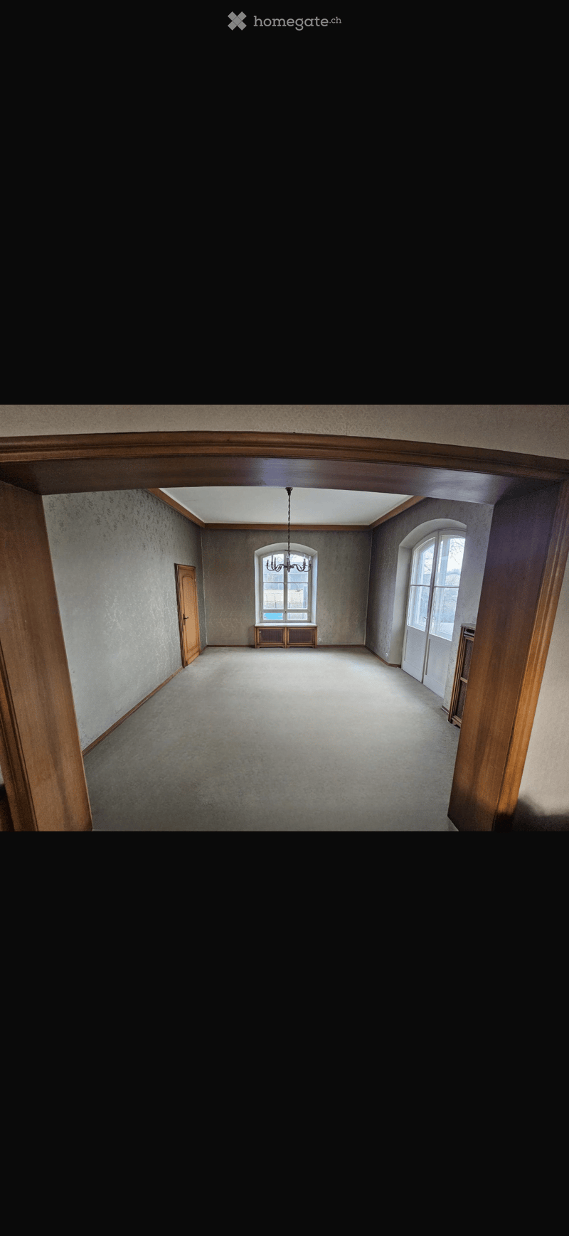 Empty room with wooden doors, carpeted floor, and large windows. No furniture or equipment present.