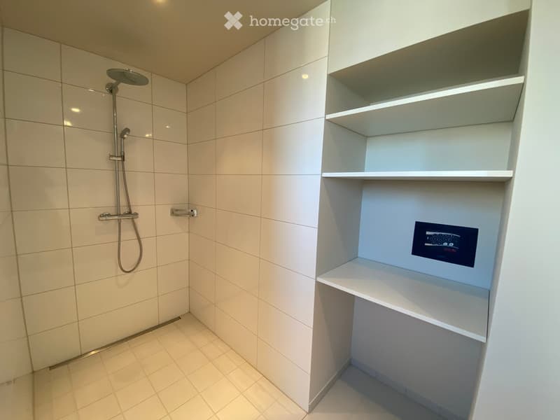 Modern shower area with white tiles, built-in shelves, and a control panel for water settings.