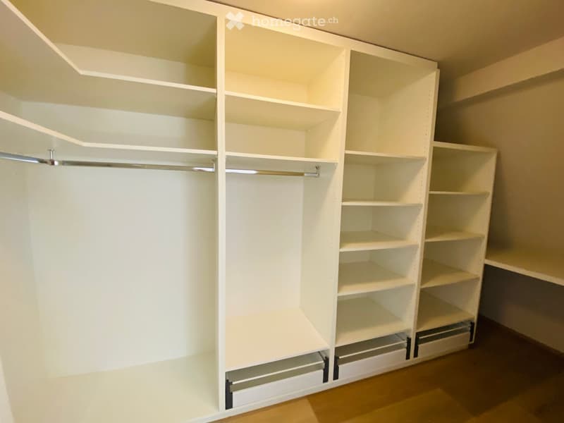 Empty closet with white built-in shelving and hanging rods, no items stored inside.
