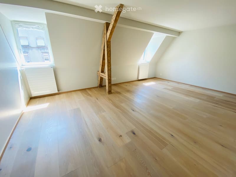 Empty attic room with wooden flooring, slanted ceilings, and skylight windows. No furniture or equipment present.