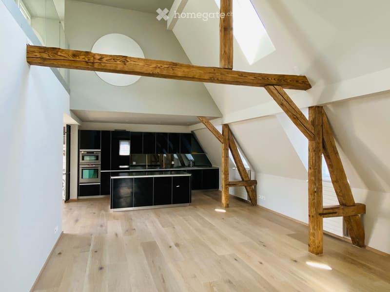 Modern kitchen with dark cabinets, stainless steel oven, and wooden beams in an open loft space.