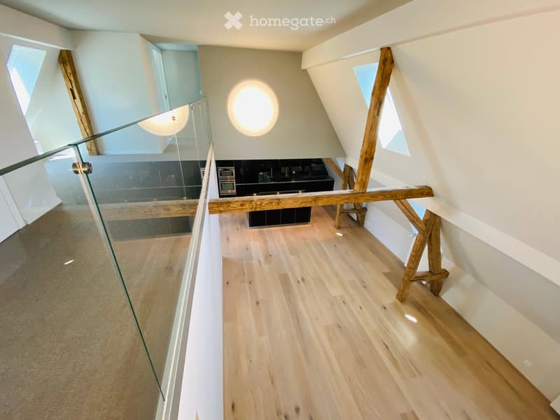 Modern hallway with wooden flooring, glass railing, and visible kitchen area in the background.