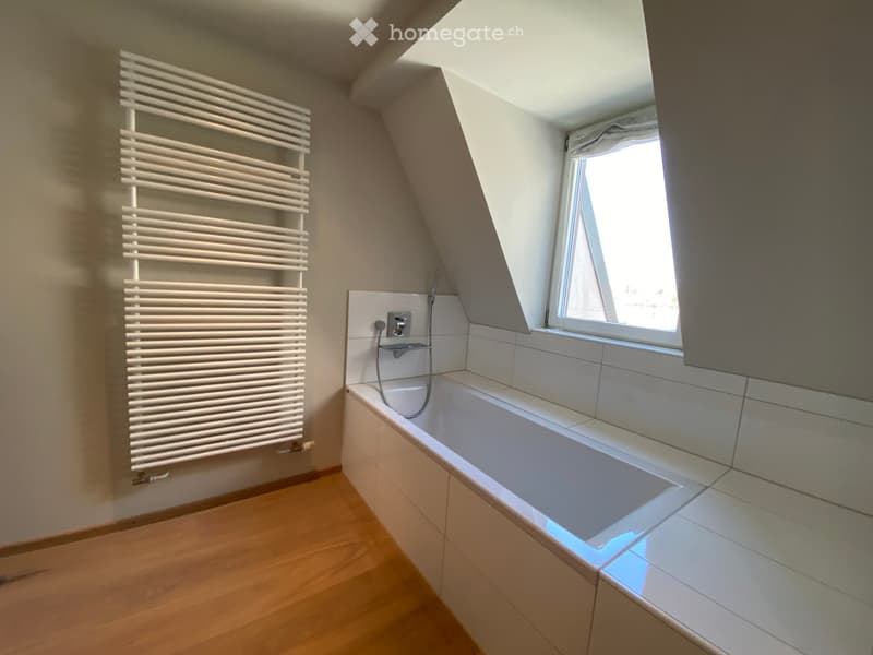 Modern bathroom with a bathtub, radiator, and a window letting in natural light.
