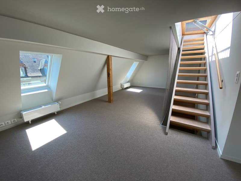 Empty attic space with wooden staircase leading up, skylight windows, and carpeted floor.