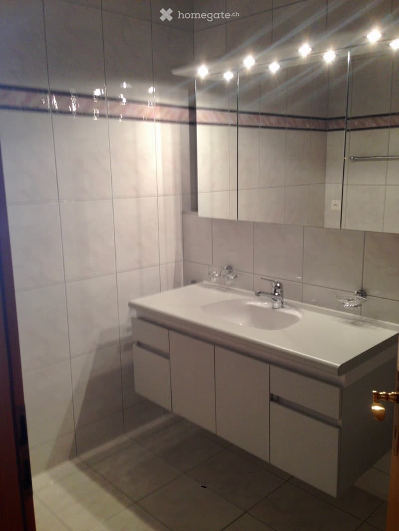 Modern bathroom with a white sink, faucet, mirrored cabinet, and tiled walls.