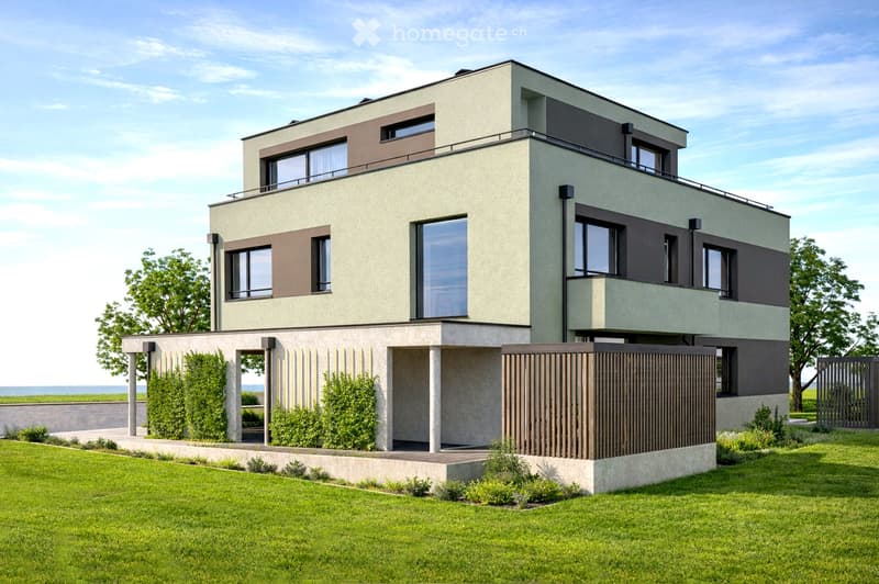 Modern two-story house with a raised ground floor, large windows, and a balcony on the upper level. The house features a combination of light and dark tones, surrounded by a well-maintained lawn and greenery.