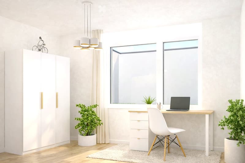 Modern, well-lit room with a white desk, laptop, chair, cabinet, and plants near the windows.