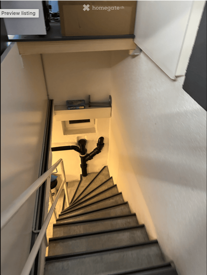 Spiral staircase with metal railing, white walls, and a small shelf on the landing.