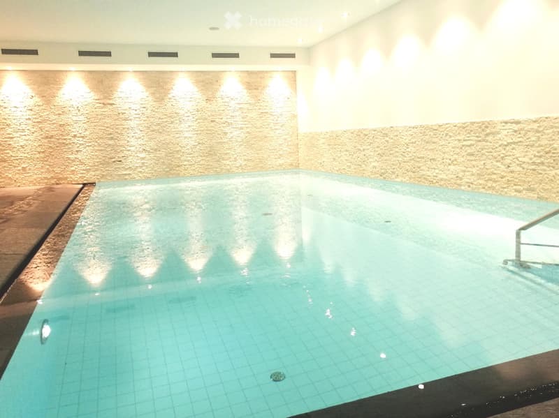 Empty swimming pool with white tiled walls, black trim, illuminated bottom