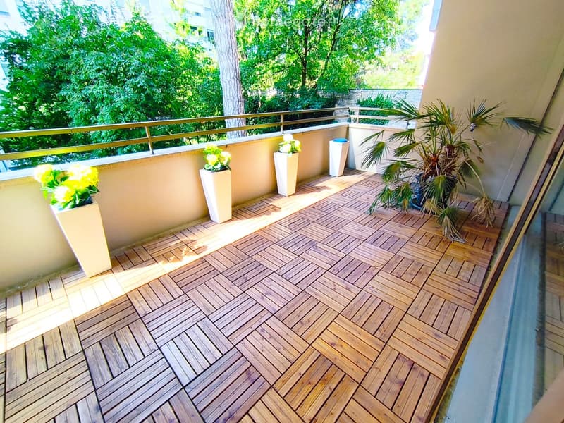 Balcony with wooden decking, potted plants, and a metal railing overlooking a green area.