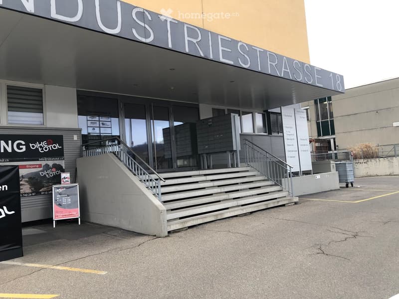 Modern building entrance with stairs, signage reading "Industriestrasse 18", and a "Bike Total" advertisement board.