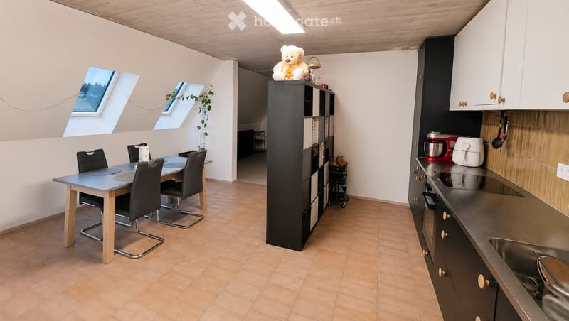 A modern, well-lit room with a dining area and kitchen. The dining area features a table with four chairs, and the kitchen includes cabinets, a sink, and various appliances.