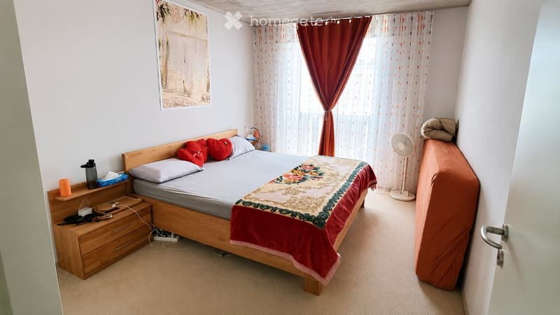 Cozy bedroom with a wooden bed, nightstand, fan, sofa, and picture frame on the wall.