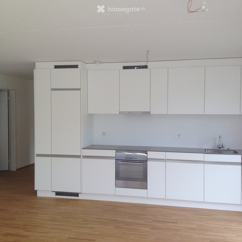Empty kitchen with white cabinets, stainless steel oven, sink, and wooden flooring.