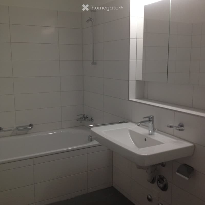 Bathroom with a bathtub, sink, and mirror, featuring tiled walls and a window above the sink.