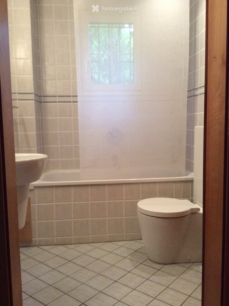 Bathroom with beige tiled walls and floor, featuring a toilet, bathtub, and sink.