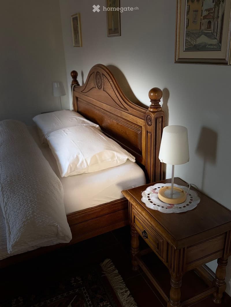 Cozy bedroom with a wooden bed, nightstand, lamp, and framed pictures on the wall.