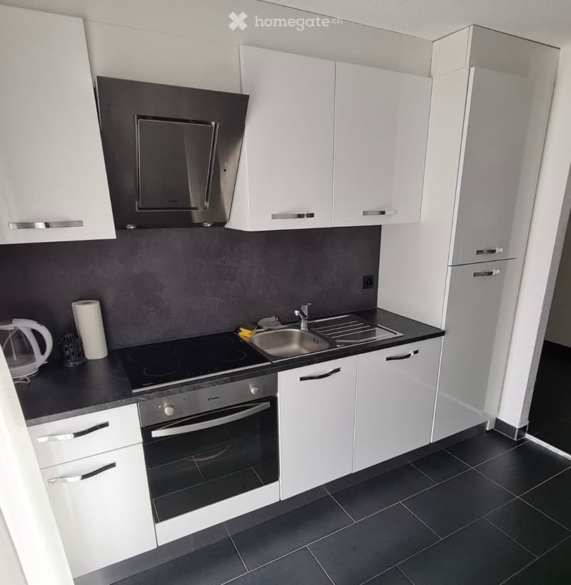 Modern kitchen with white cabinets, black countertops, and stainless steel appliances including an oven, sink, and faucet. A small electric kettle and a candle are placed on the counter.