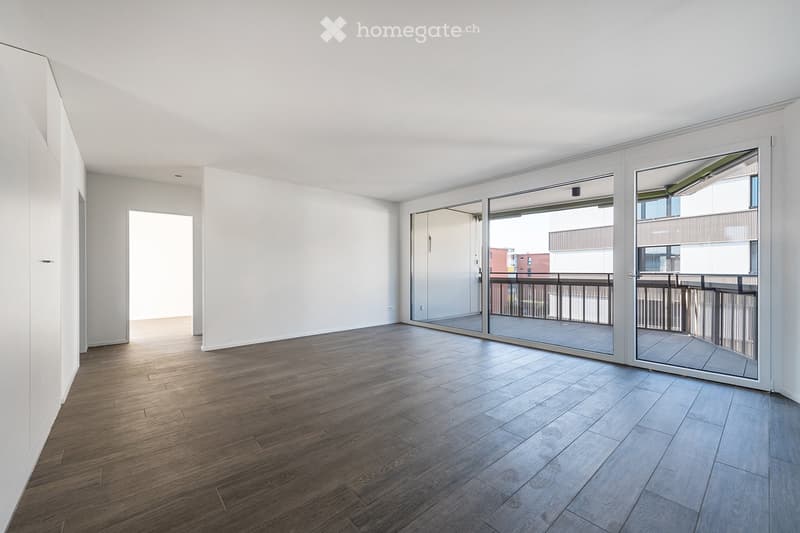 Empty room with wooden flooring, white walls, and large sliding glass doors leading to a balcony.