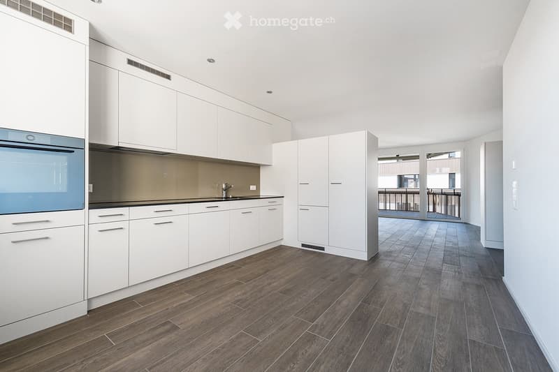 Modern kitchen with white cabinets, dark countertops, and wooden flooring. Features a sink with a modern faucet and built-in appliances.